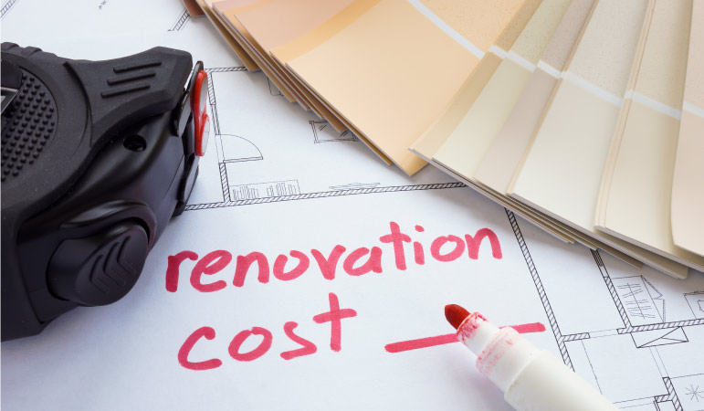 The note “renovation cost ___” written in red on a home’s blueprint. There are a variety of paint chips and a tape measure nearby.