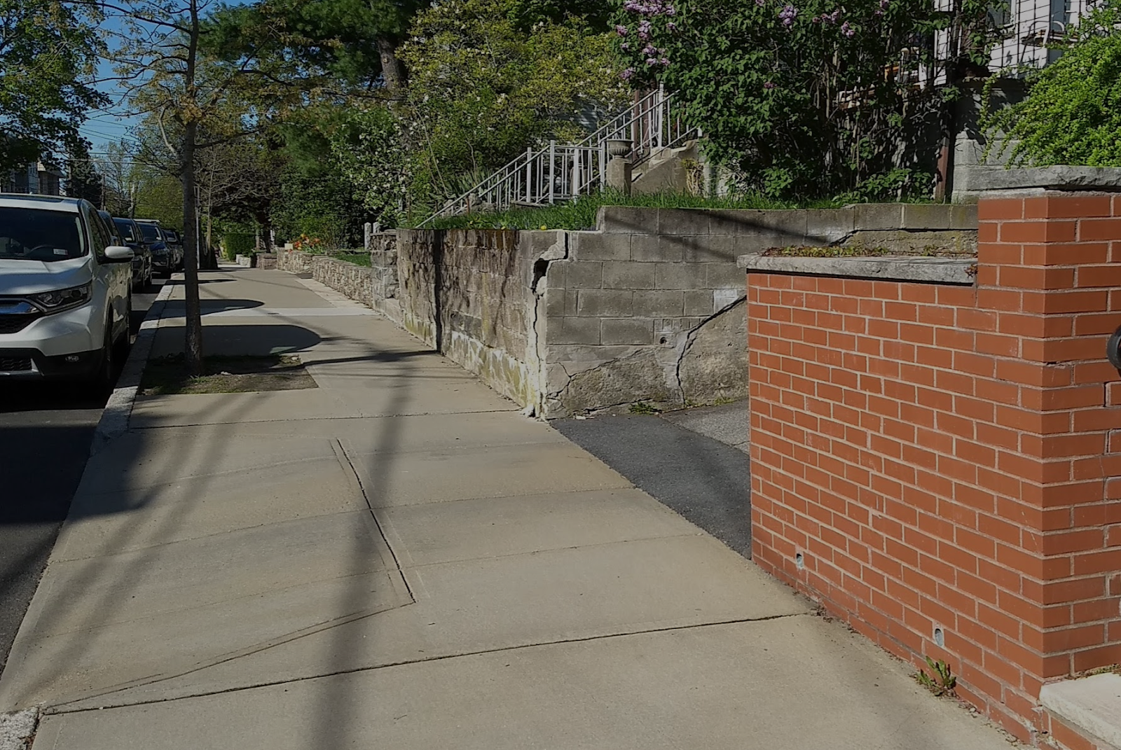 Blind driveway example with no way to see cars backing out due to a tall retaining wall constructed at a right angle and up to the sidewalk