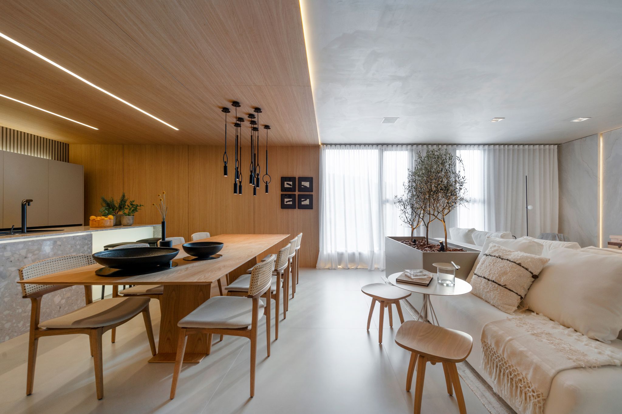 Sala integrado a cozinha com piso de madeira, mesa de jantar de madeira, cadeiras de madeira com estofado cinza, parte da cozinha com parede e teto revestido de madeira