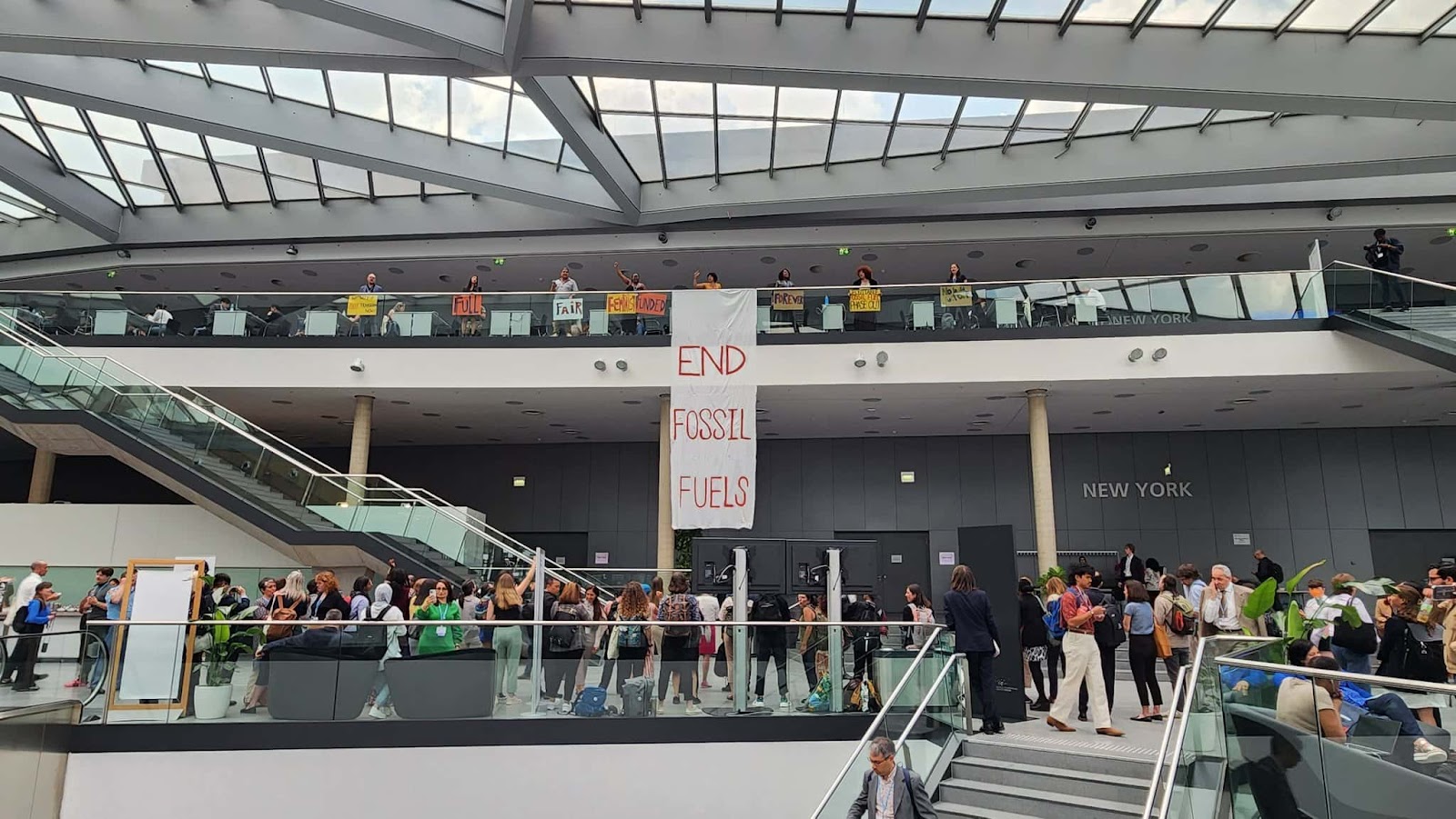 Activists drop a banner saying End Fossil Fuels inside the large foyer of the UN building