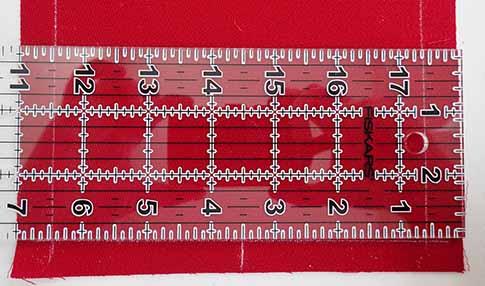 A piece of red wool fabric with a clear ruler on top. Two thin white lines indicate 1/2" from each edge for a seam allowance.