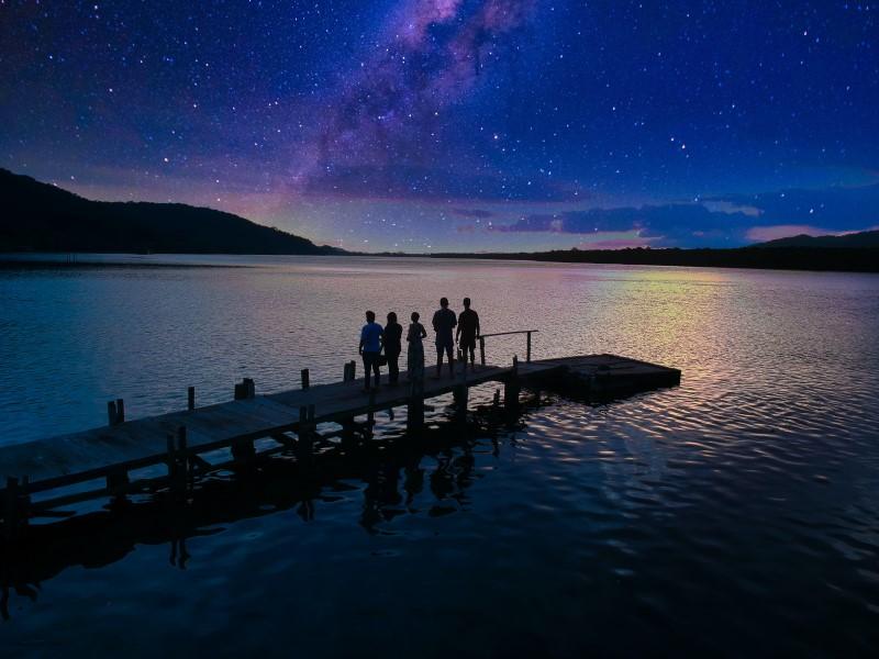 A group of people standing on a dock over water with a starry sky above

Description automatically generated with low confidence