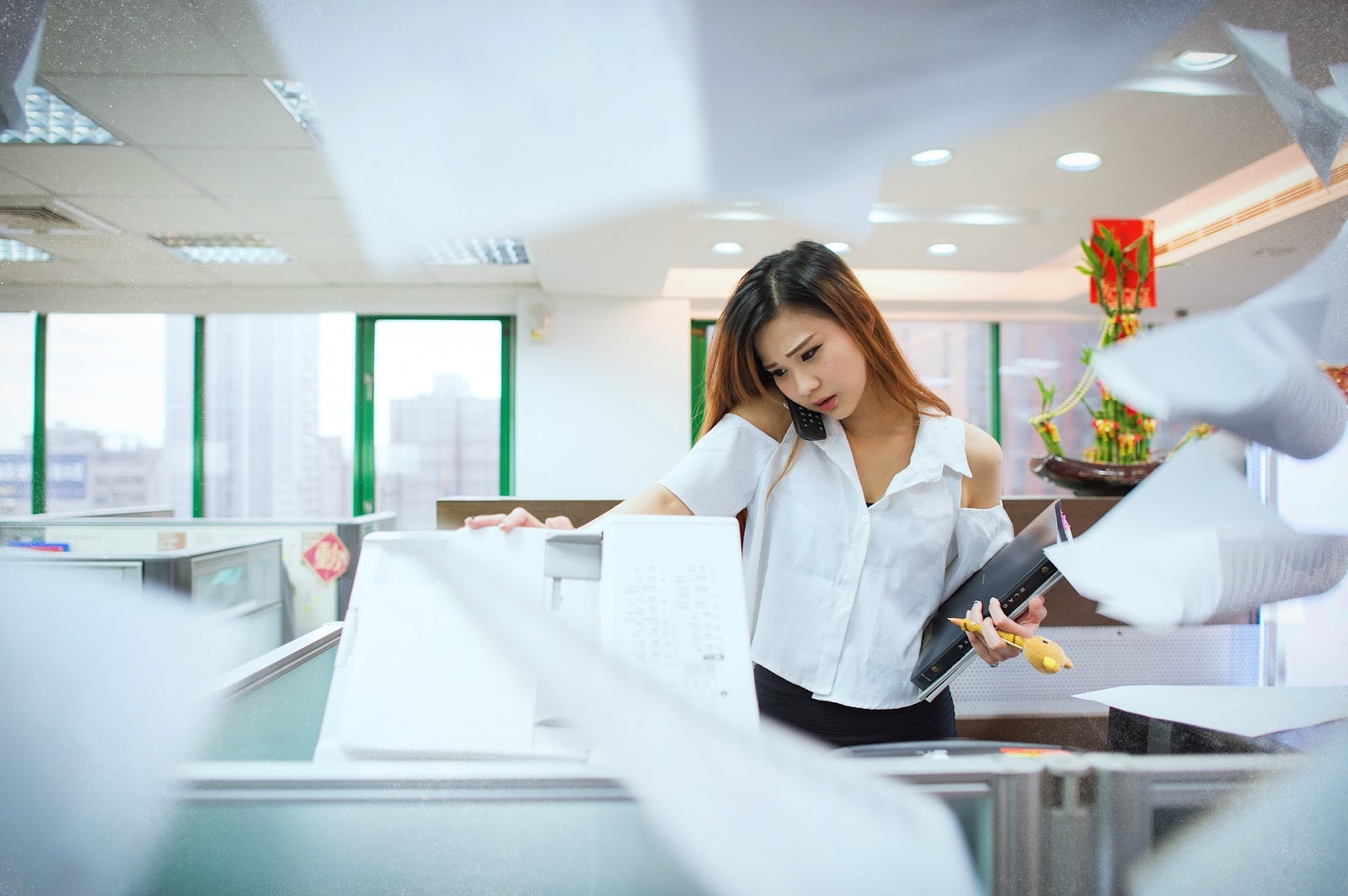 A picture of a busy female office worker, carrying notes, making copies, and talking on the phone