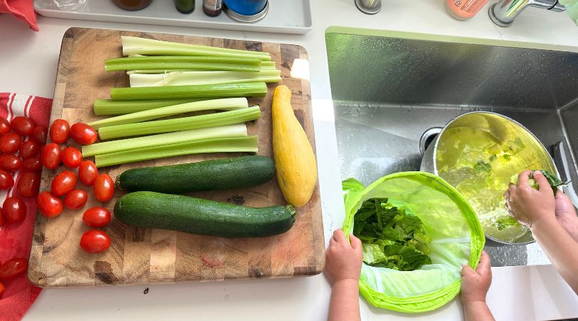Two small kids putting lettuce in a saladzilla, next to a cutting board with produce