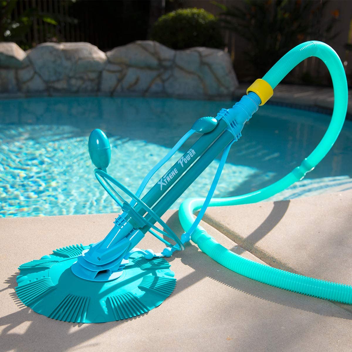 a light blue automatic pool vacuum with a circular suction and long hose next to an inground pool