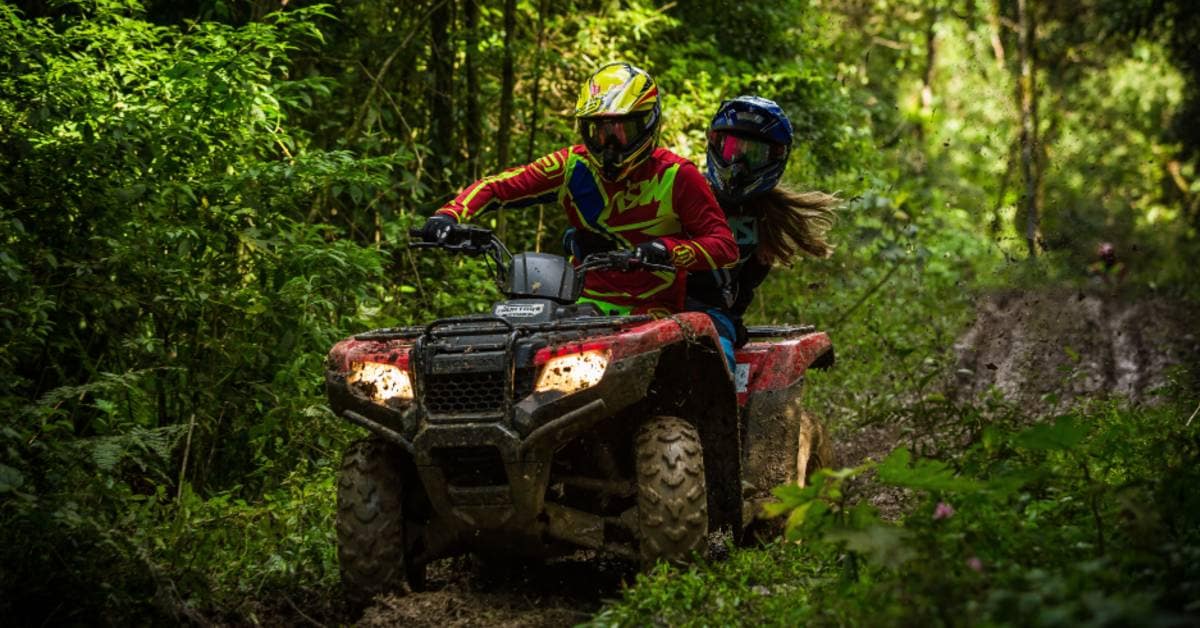 Adventurous couple explores the great outdoors on an ATV, riding through lush green trails in full riding gear