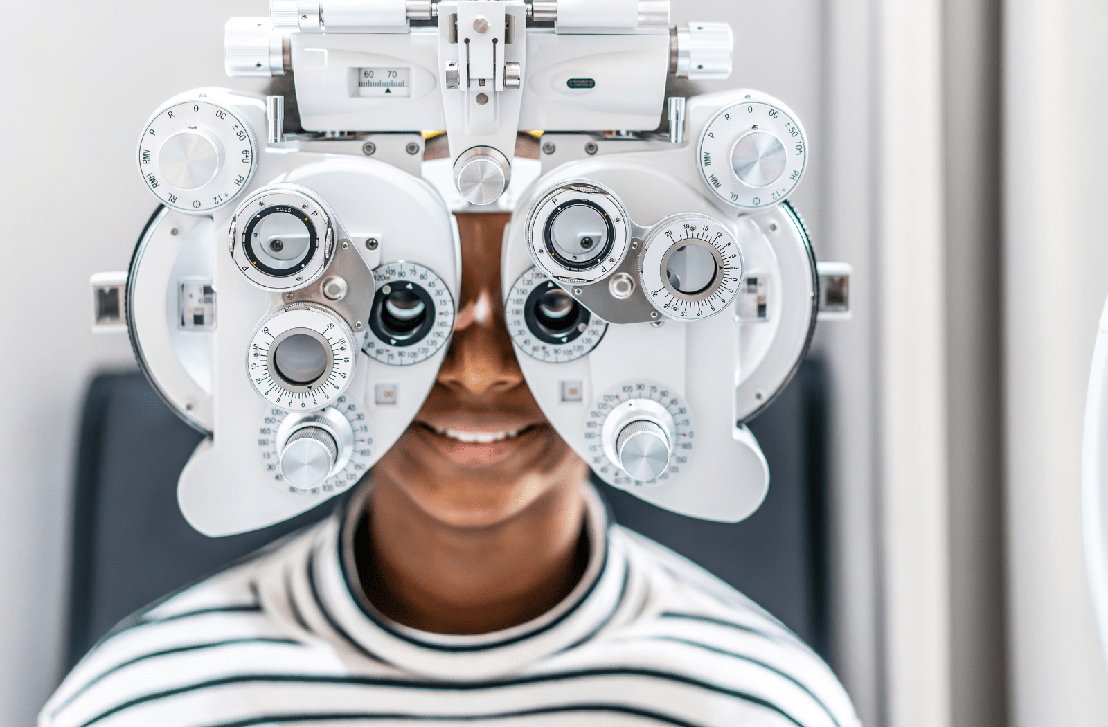 A young man sitting and smiling behind a phoropter at the optometrists office