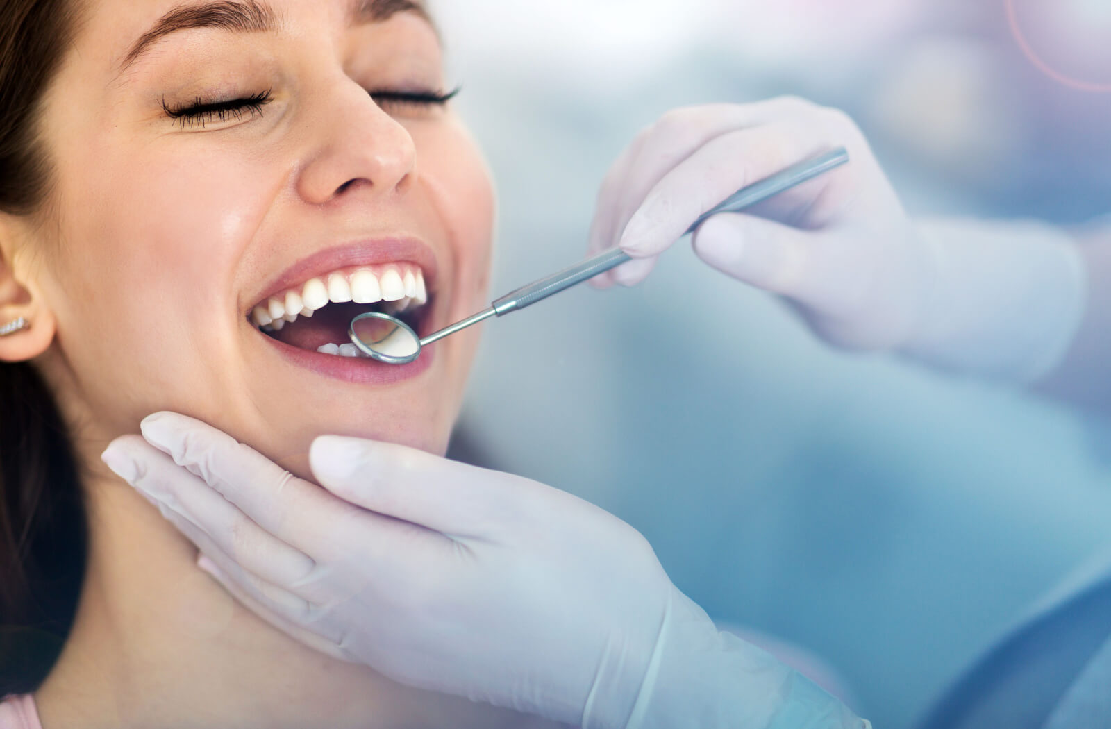 A close-up of a woman having her teeth examined by a dentist with a mouth mirror