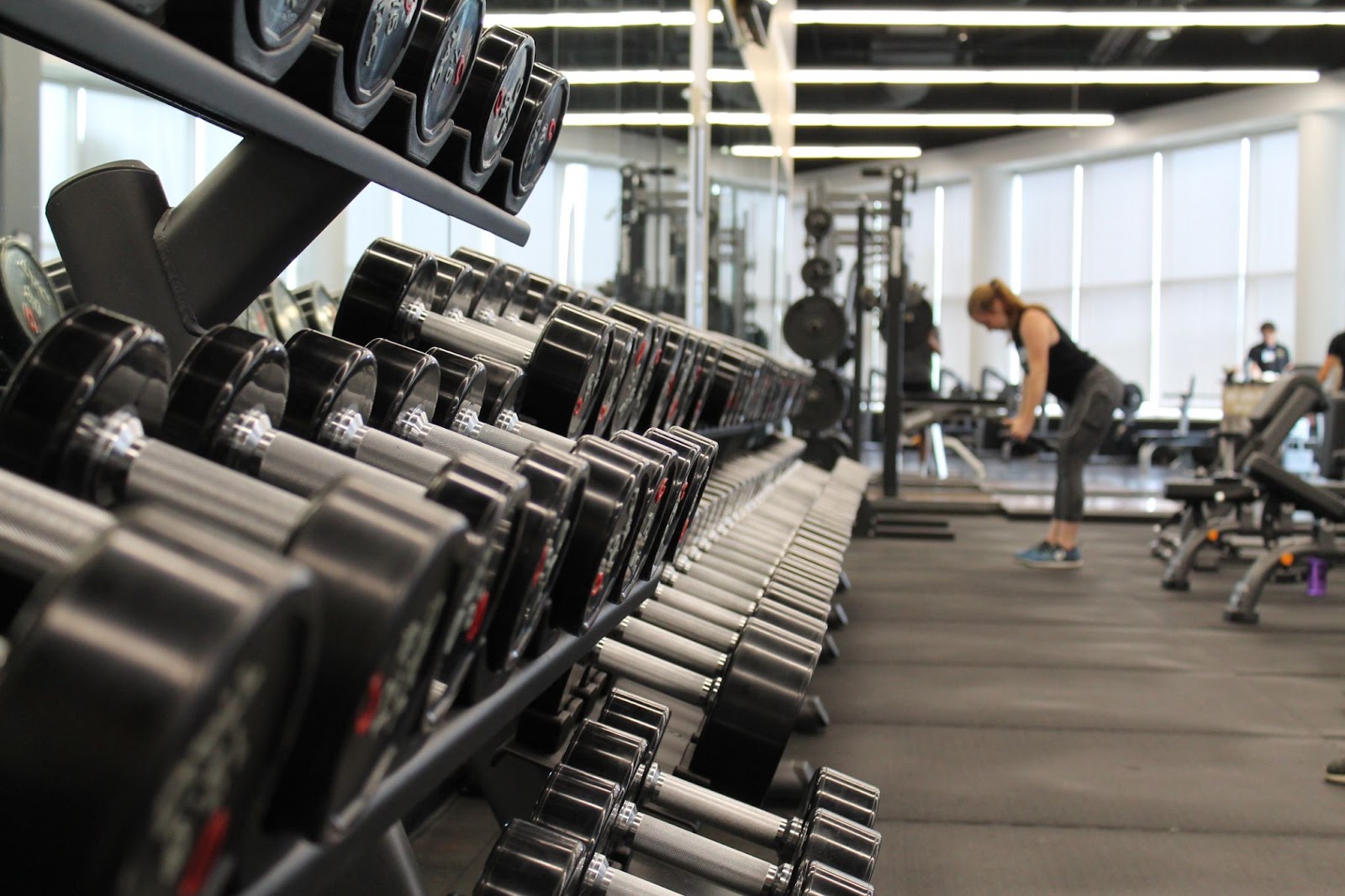 Woman working out in front of dumbbell rack in fitness studio.