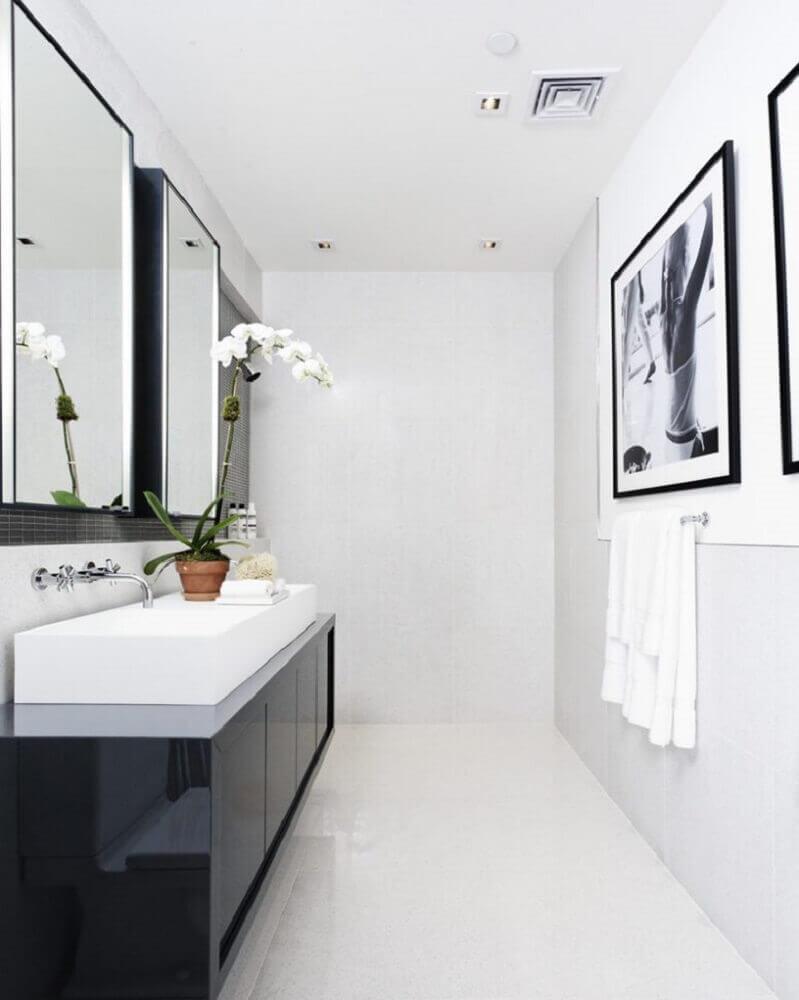 banheiro com paredes, piso e teto brancos, quadros decorativos preto e branco, armário preto com cuba branca e espelhos com moldura preta.