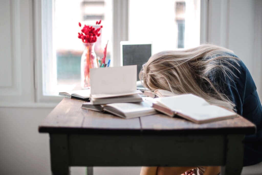 Woman-drops-head-on-table-surrounded-by-notebooks