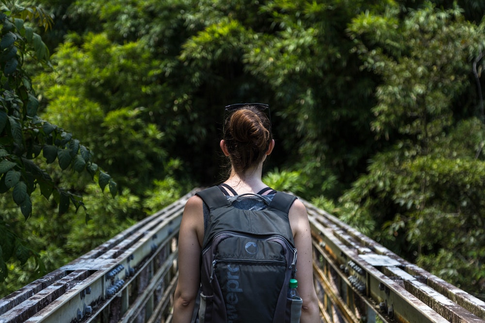 Hiker in a backpack walks along a narrow bridge in the jungle