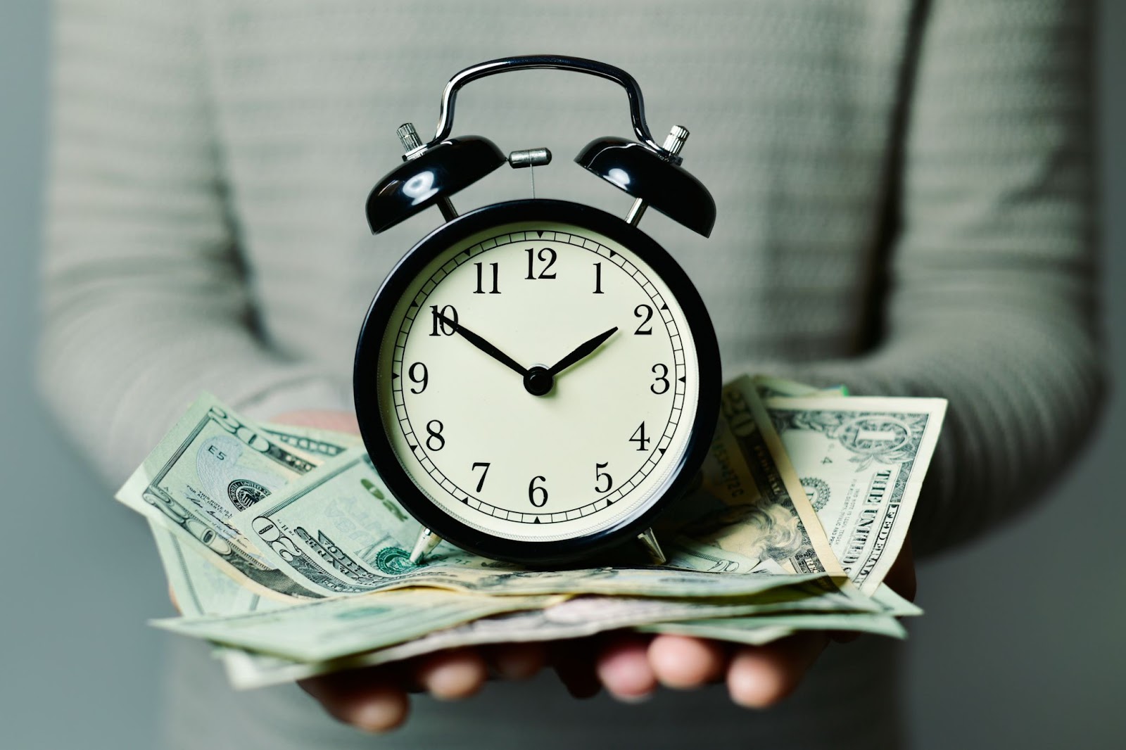 A person holding a pile of cash with a clock sitting on top of it, in reference to a digital marketing agency saving a business money. 
