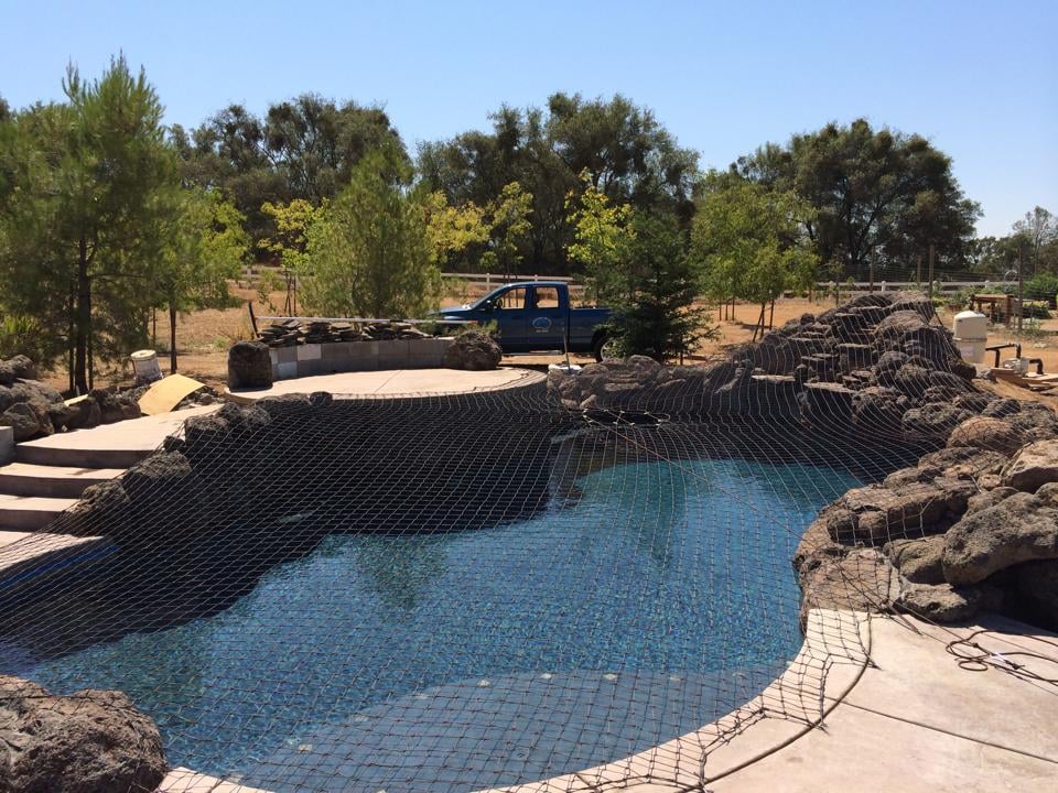 Tan swimming pool safety net installed on a backyard pool with rock formations
