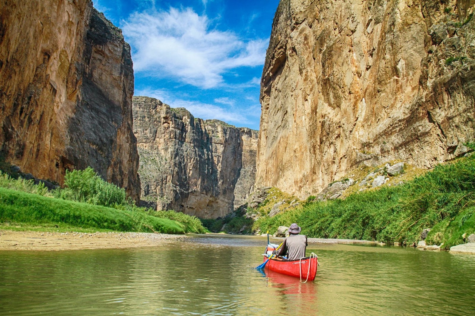 A person in a red canoe on a river, surrounded by large cliffs on both sides.