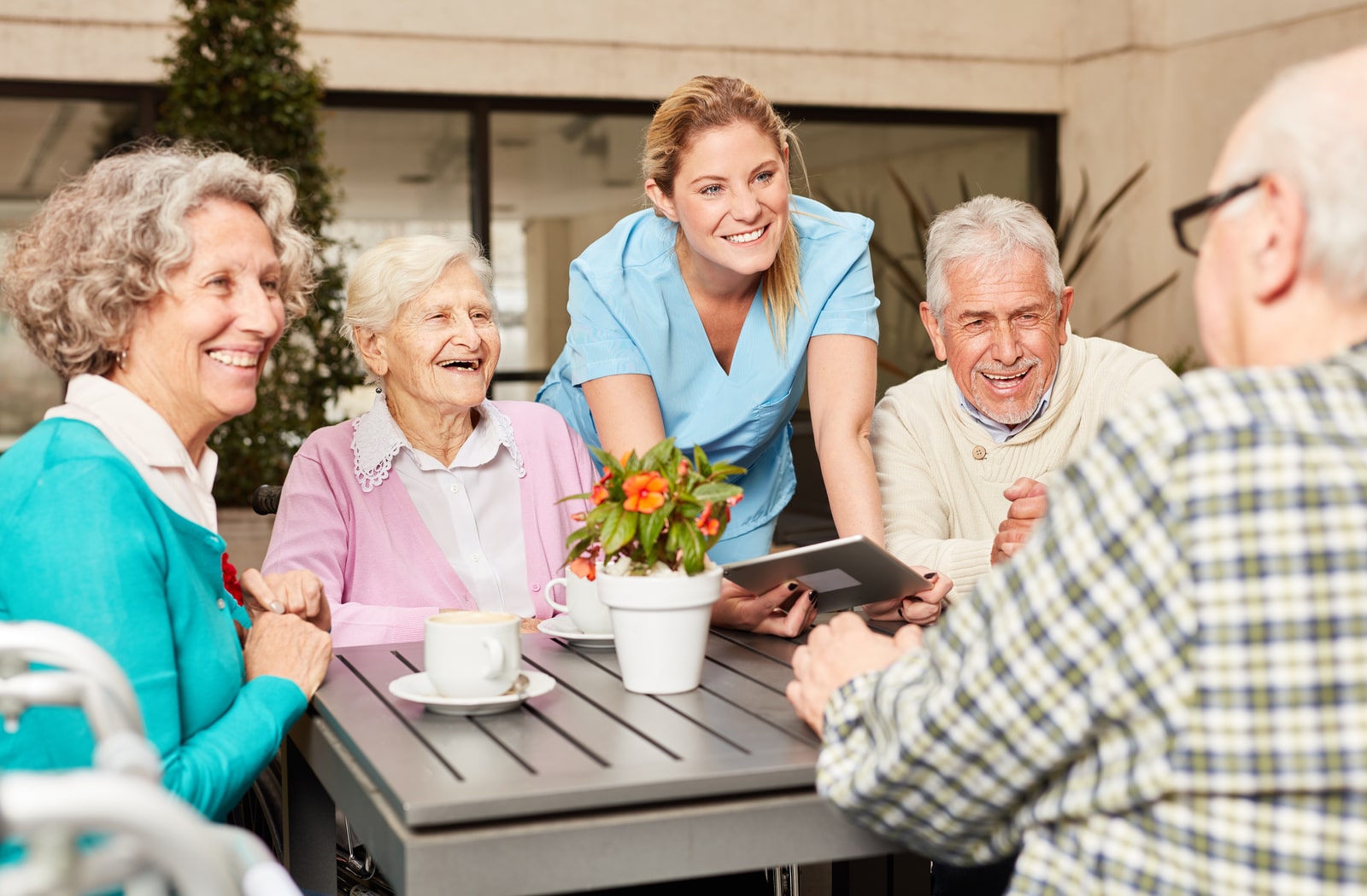 A group of seniors talking and drinking coffee, while a young female nurse talks with them as well