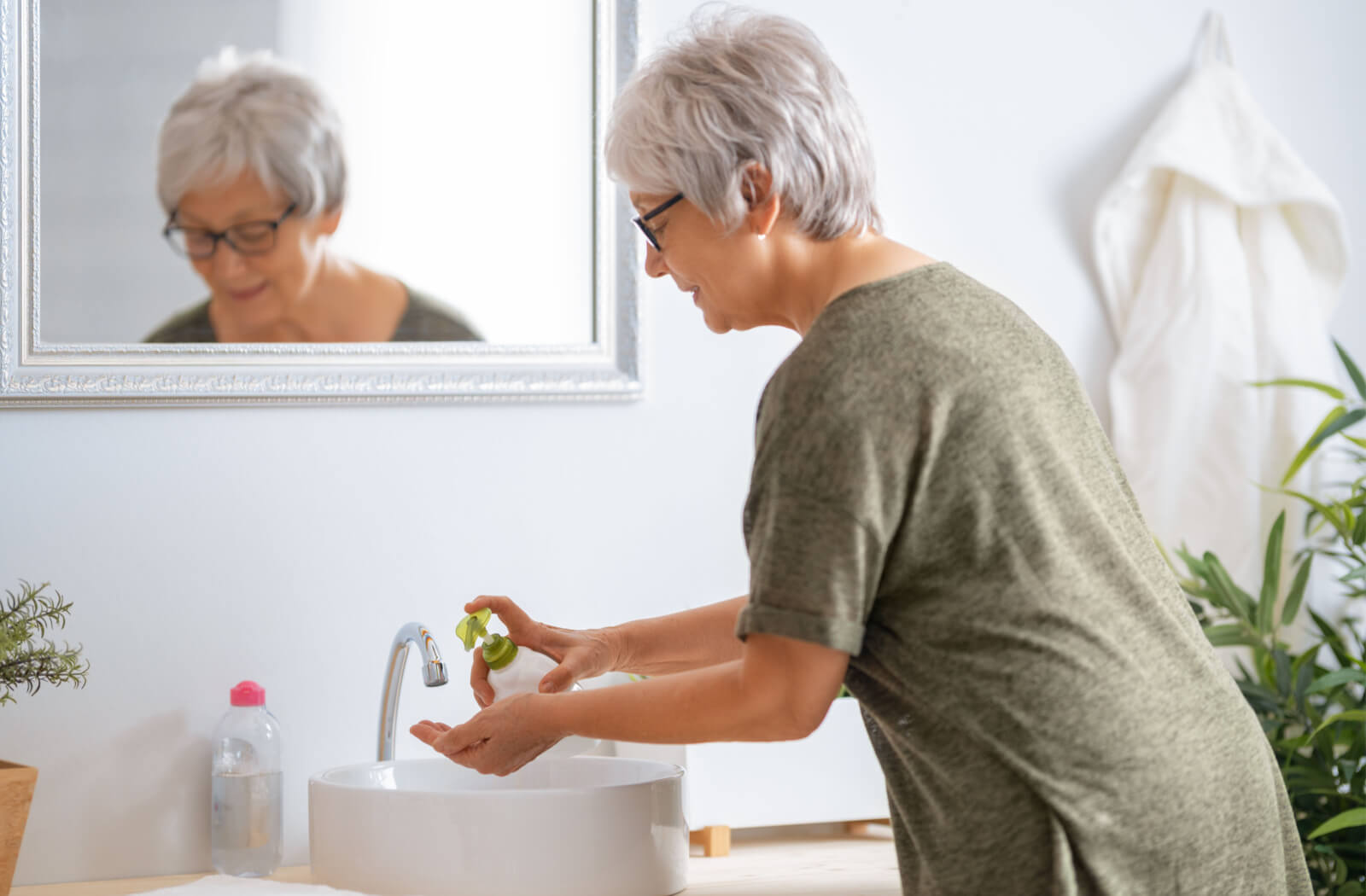 A senior woman smiling and washing her hands with hand soap in the bathroom.