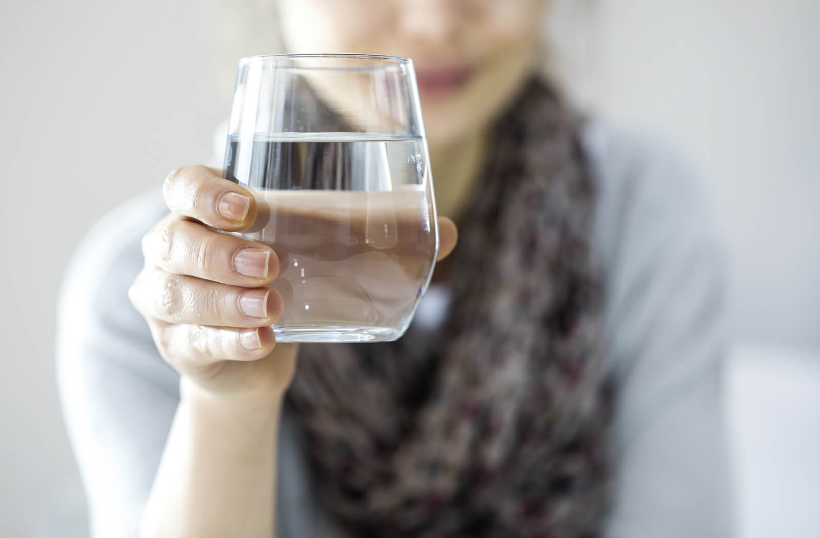 a woman holds a glass of water which she will drink to stay hydrated and minimize dry eye