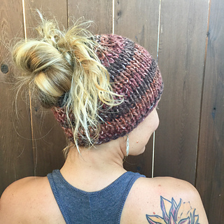 chunky striped messy bun knit beanie modeled in front of a wooden fence