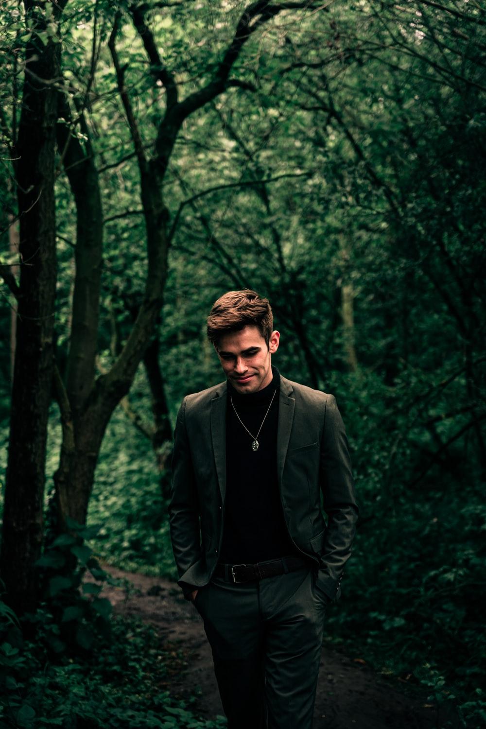 man in black suit jacket standing in forest during daytime