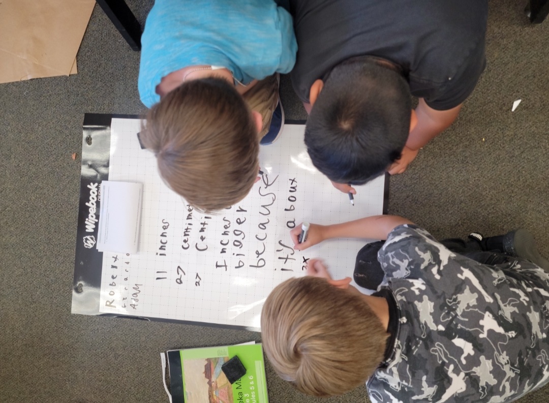 Three students using dry erase markers on a Wipebook Flipchart to solve math problems collaboratively.