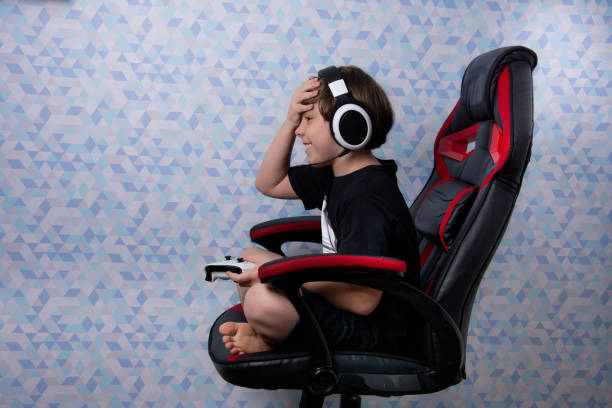 boy sitting in gamer chair with headset and video game control boy sitting in gamer chair with headset and video game control gaming chair stock pictures, royalty-free photos & images