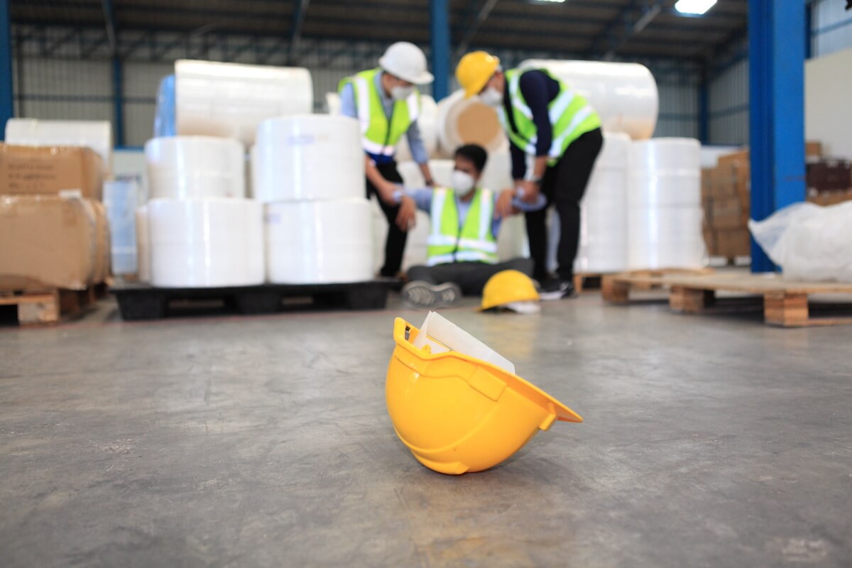 Job safety analysis: hard hat on the floor and a worker that had an accident in the background