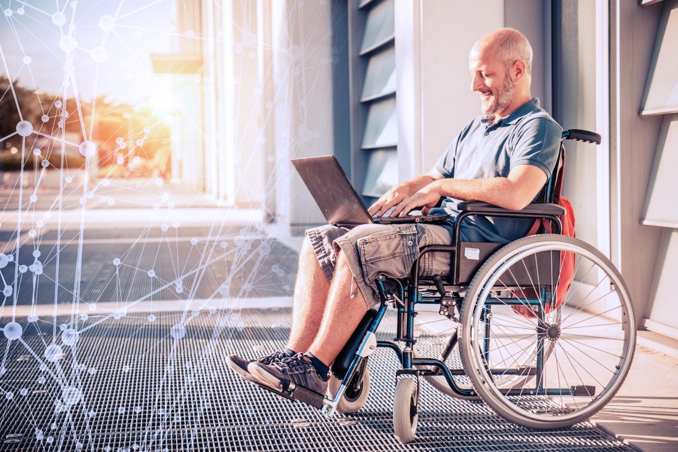 Disabled man sitting in wheelchair with a laptop on his lap.