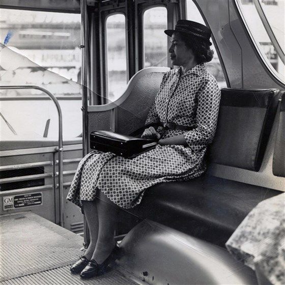 Rosa Parks, mulher negra de vestido e chapéu, sentada no banco de ônibus.