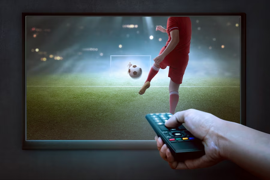 a hand holding a remote control with a television displaying a football game