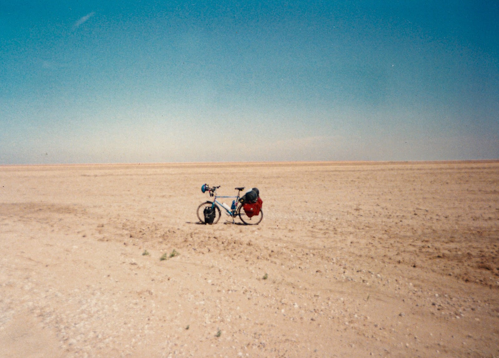 A bicycle is in a dirt field with no contour that stretches into the distance under a blue cloudless sky. 