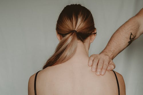 Free Back view of anonymous female sitting on white background while being touched by strong faceless abusive man in light room Stock Photo