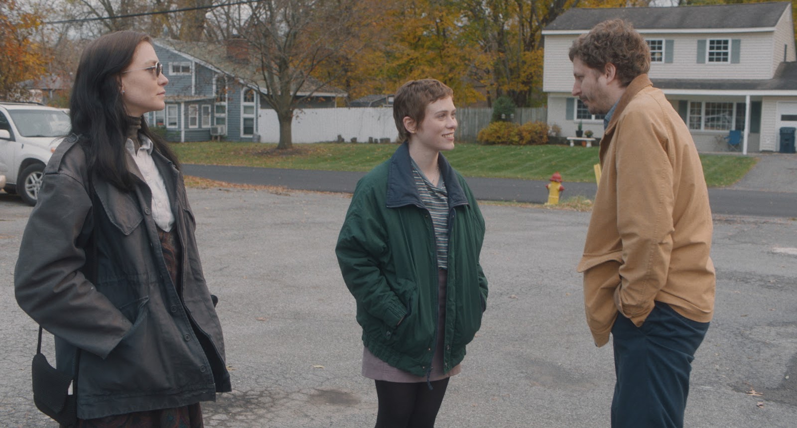 From the film The Adults, two women are talking to a man, played by Michael Cera, while standing on the cement outside of a suburban neighborhood.