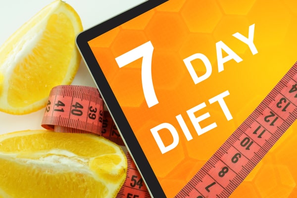 Two slices of lemon with a board that says "7 day diet" surrounded by a red tape measure