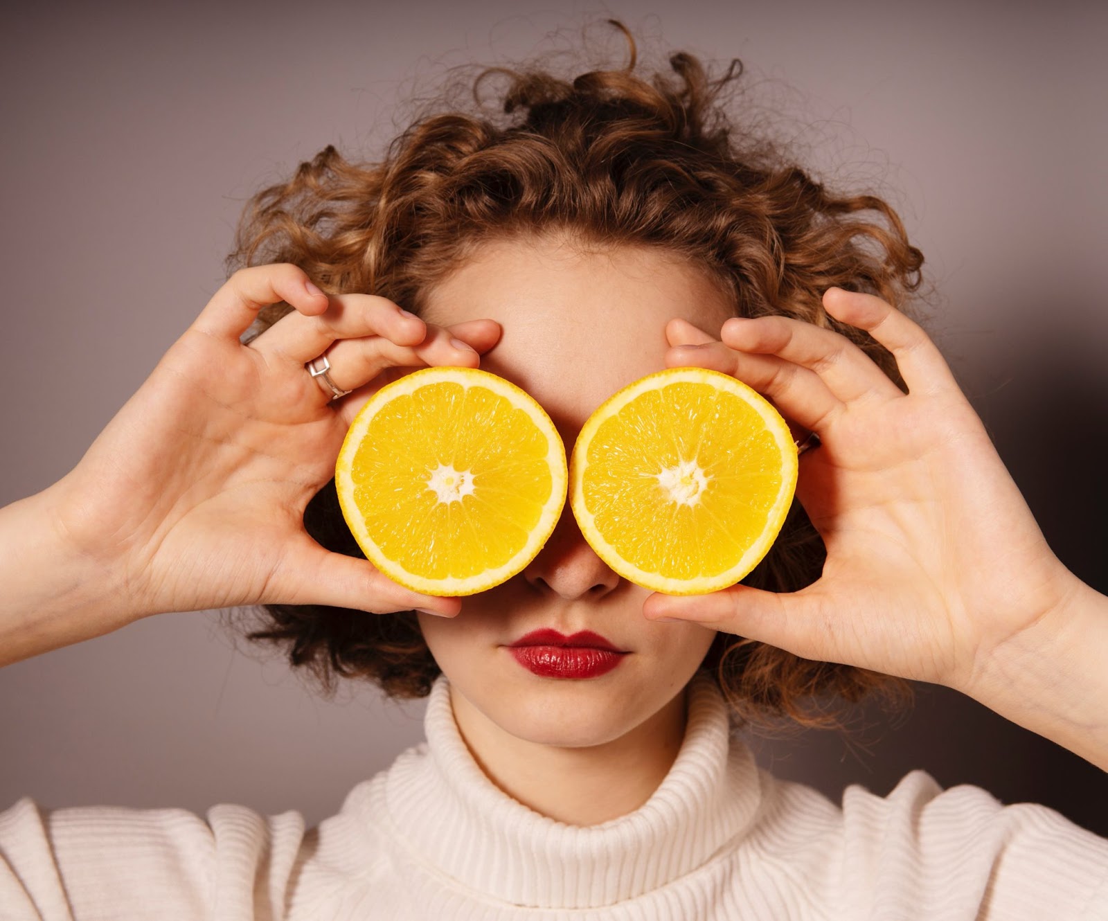 A picture of a woman holding to orange halves in front of her eyes.