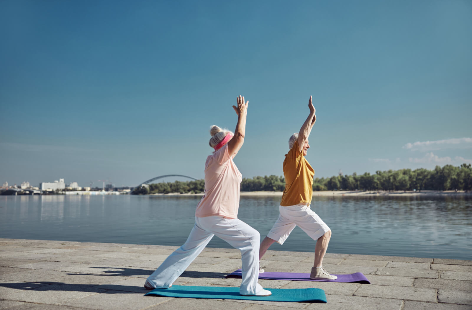 A senior man and a senior woman doing an overhead arm raise exercises outdoors.