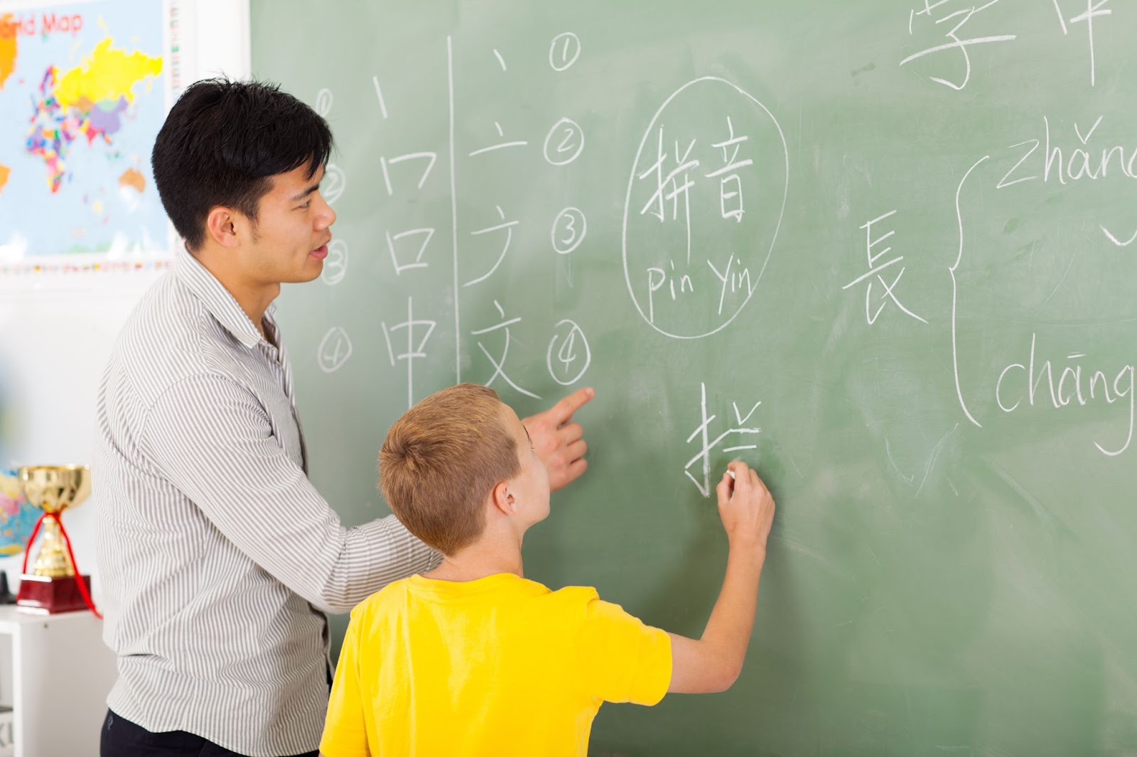A male teacher teaching a young boy to write Chinese on the board.