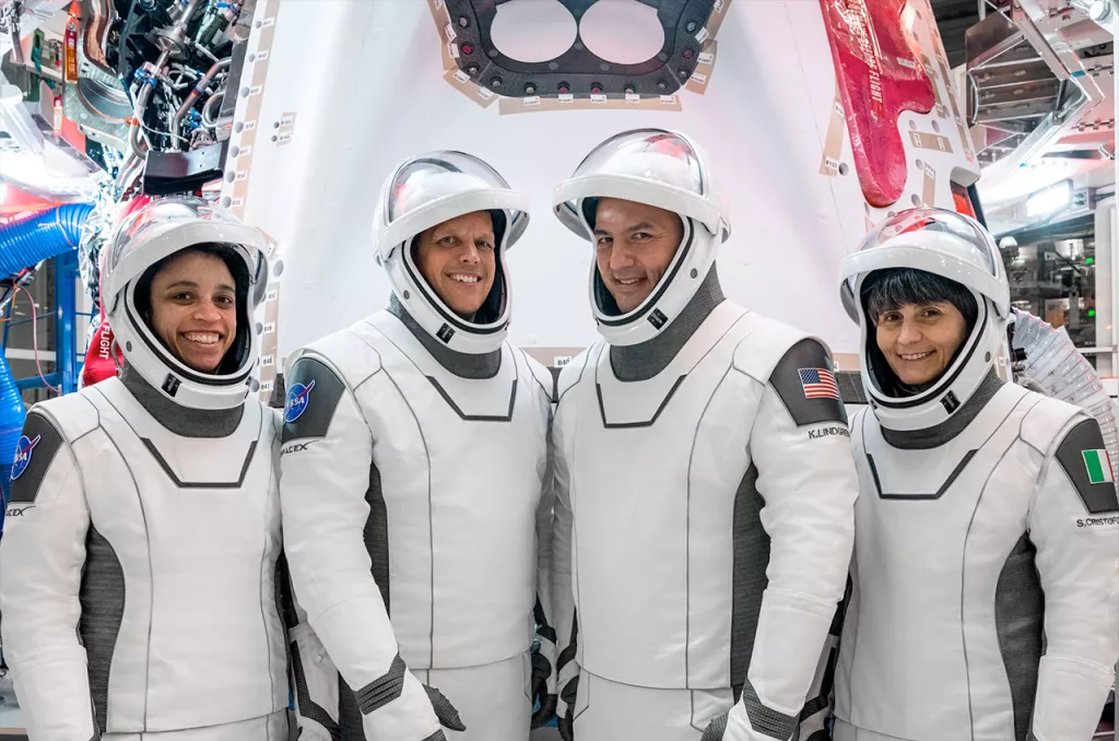 Four astronauts pose and smile in astronaut gear. 