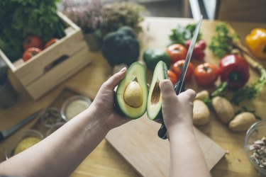 Top view of a person cutting an avocado among other healthy fruits and vegetables
