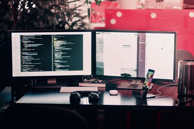 a table with two black desktop monitors, a phone, and a pair of headphones on it