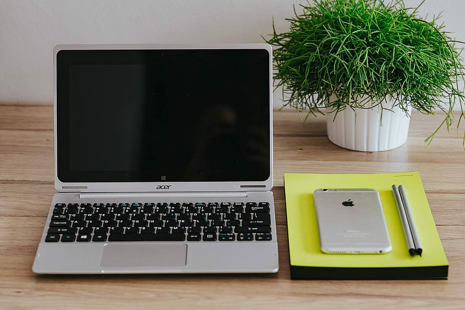 This image shows the Acer Nitro 5 with iPhone, notebooks and artificial plant tree in the table.