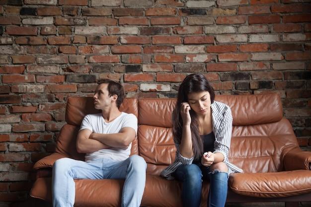 Casal chateado frustrado depois de briga sobre o que se divide na união estável sentado no sofá em casa