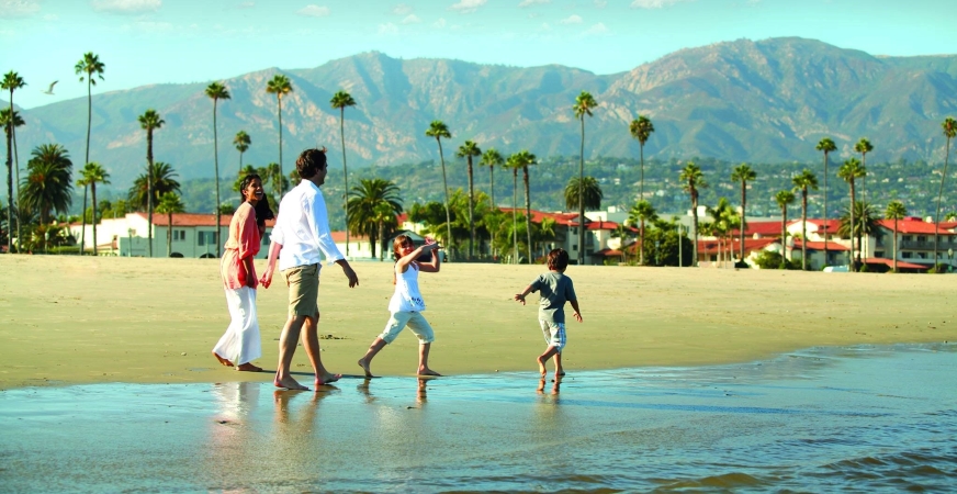 A family of four walking on one of the Santa Barbara beaches. The mountains can be seen in the background.