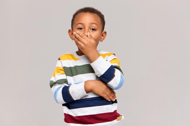 Emotional cute african american boy expressing surprise or astonishment, covering mouth with hand as sign of shock or secrecy, keeping still tongue in head. true human emotions and reaction Free Photo