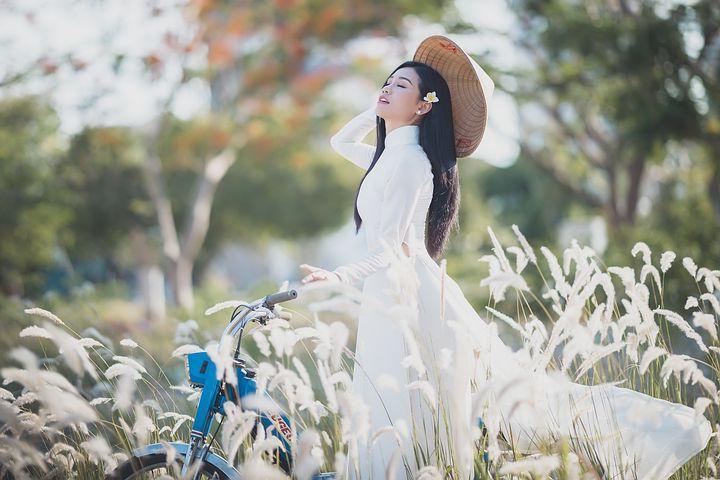 A person in a white dress and hat standing next to a blue bicycle

Description automatically generated with low confidence