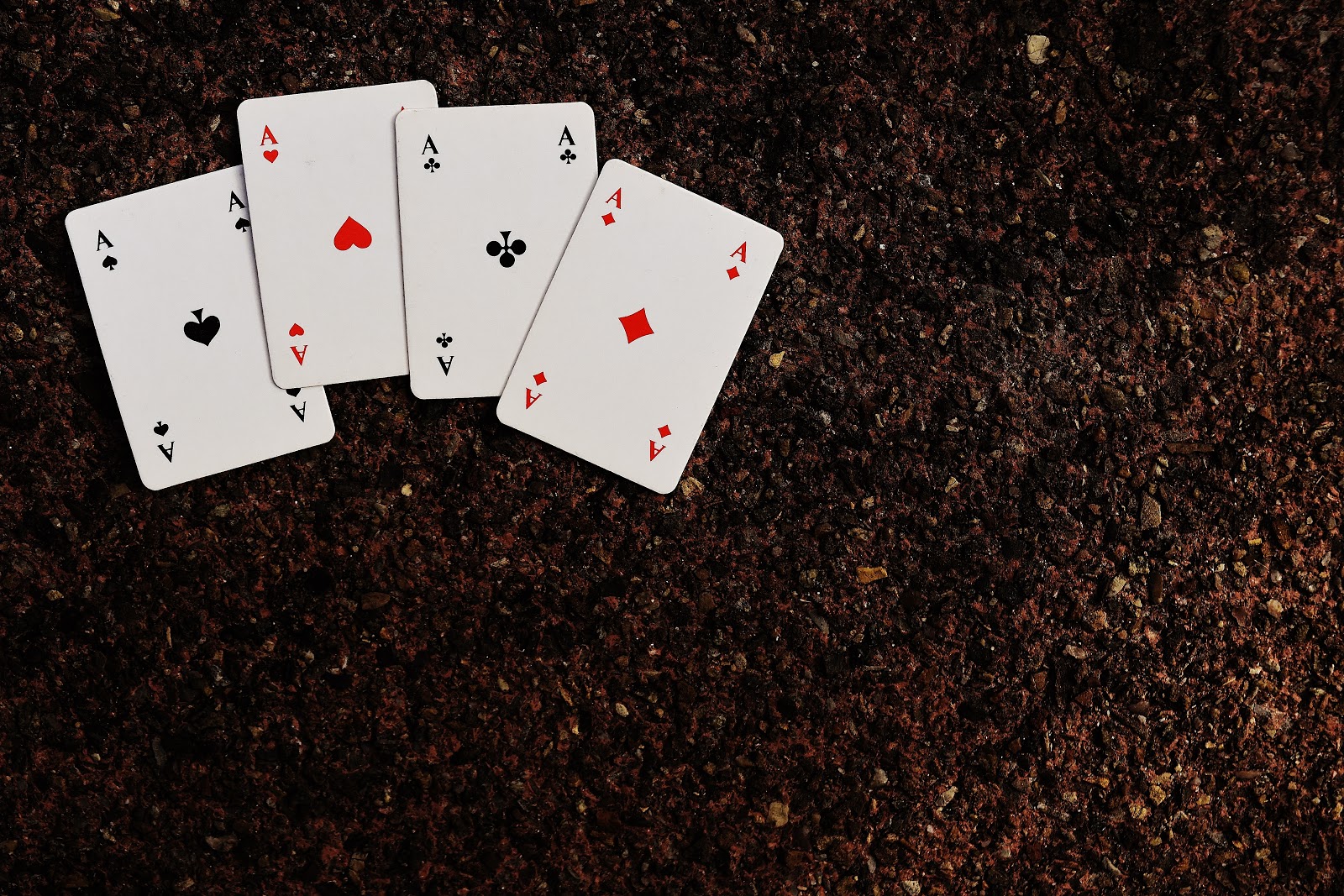 Four ace playing cards lying on brown ground made up of dirt and pebbles