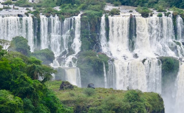 Powerful milky white water cascading down a wide set lush and green mountain found in Iguazu or Iguacu National Park in Brazil and Argentina