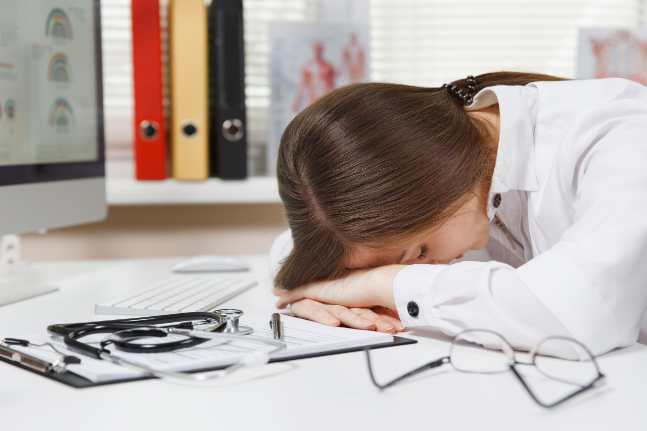 Saúde mental no trabalho: Na imagem, mulher aparentemente cansada encosta está com a cabeça encostada na mesa.