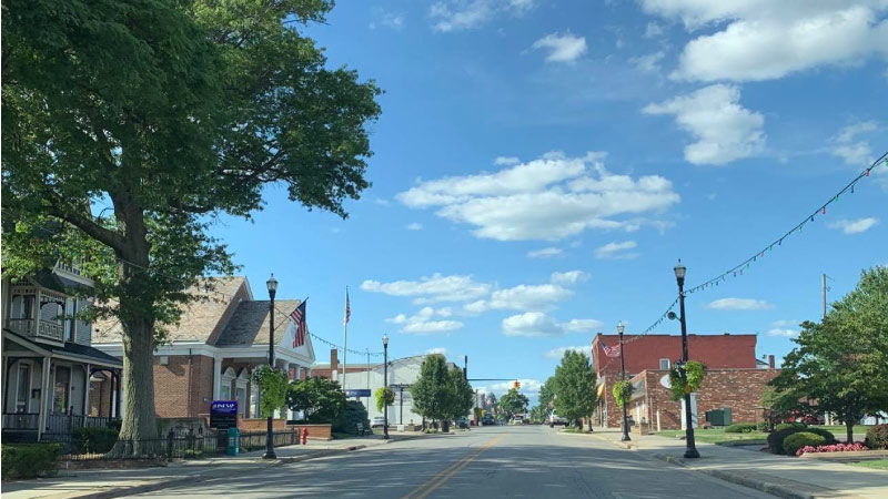 Downtown Columbiana, OH, on a beautiful summer day. The sky is blue with fluffy, white clouds and the street is lined with trees.