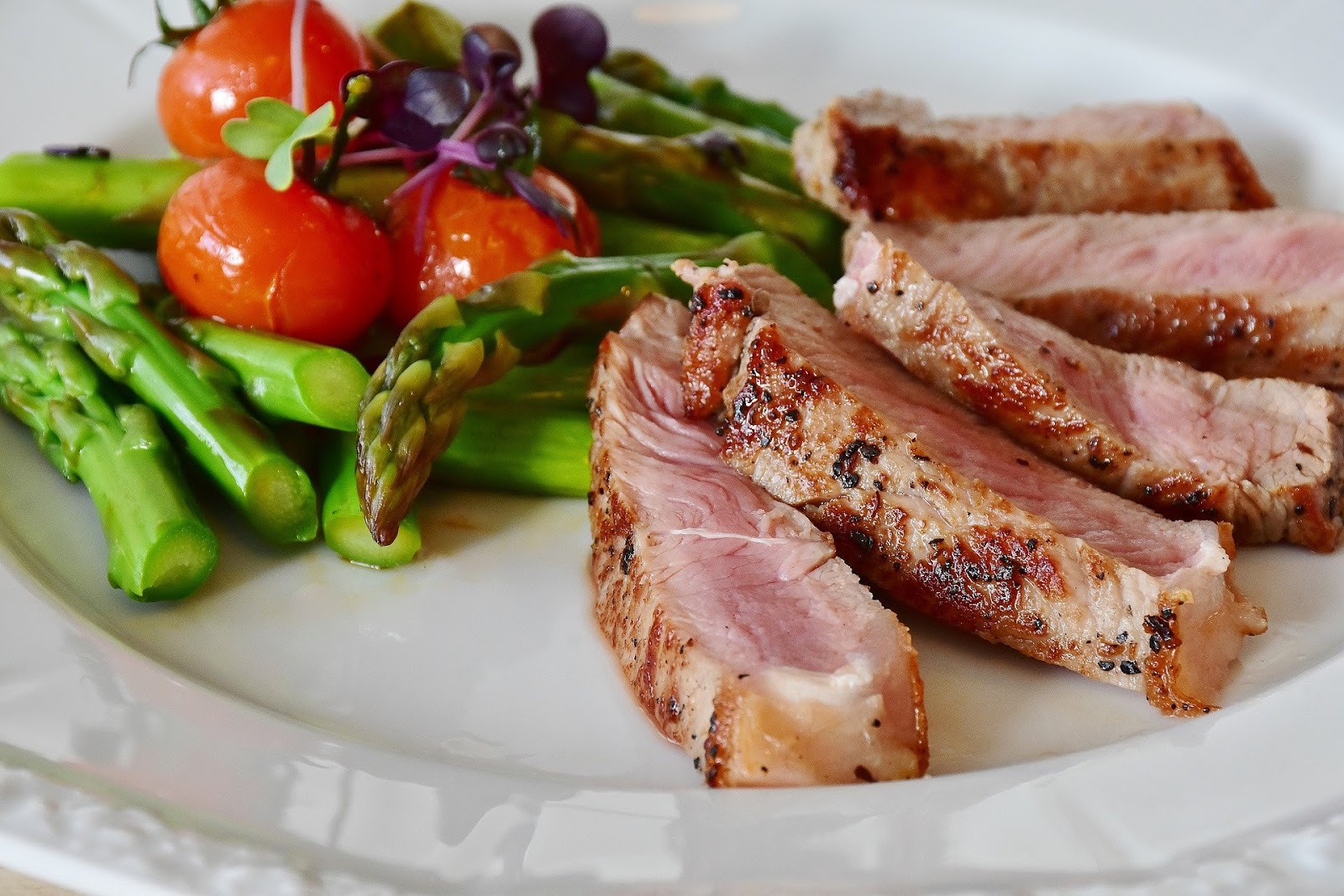 A picture of a healthy meal of pork, asparagus and cherry tomatoes.